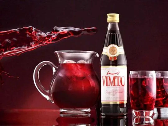Bouteille Vimto, pichet et verres remplis d’une boisson rouge avec glaçons.