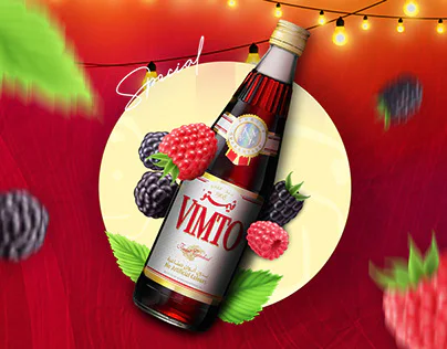 Bouteille Vimto inclinée, fruits rouges et verre servi sur fond rouge.